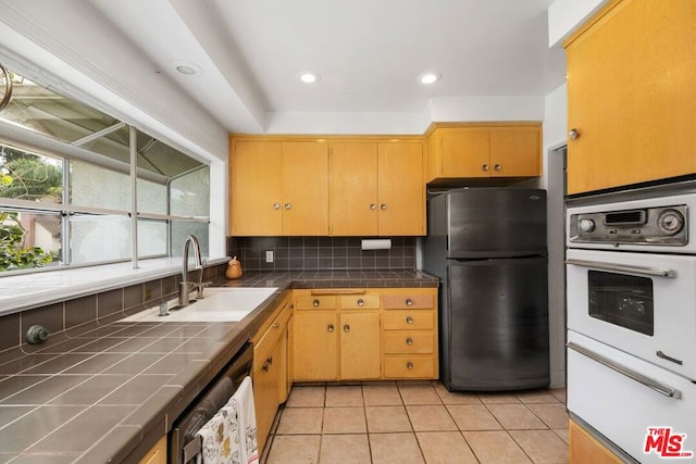 kitchen with appliances with stainless steel finishes, tasteful backsplash, sink, light tile patterned floors, and tile countertops