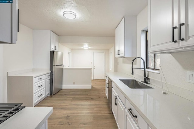 kitchen with stainless steel refrigerator, sink, light hardwood / wood-style floors, a textured ceiling, and white cabinets