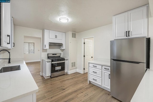 kitchen with appliances with stainless steel finishes, a textured ceiling, sink, hardwood / wood-style flooring, and white cabinetry