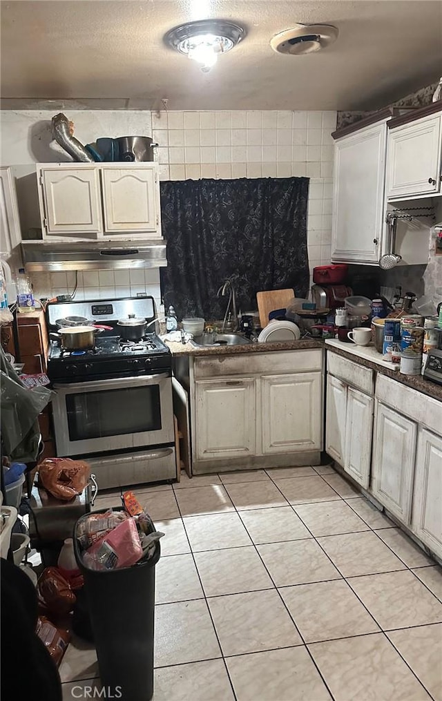 kitchen with gas stove, sink, light tile patterned floors, extractor fan, and white cabinets