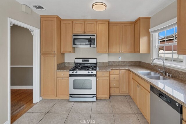 kitchen featuring appliances with stainless steel finishes, light wood-type flooring, light brown cabinetry, light stone counters, and sink