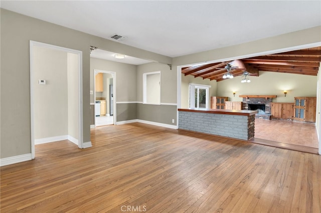 unfurnished living room featuring lofted ceiling with beams, hardwood / wood-style flooring, a brick fireplace, and ceiling fan