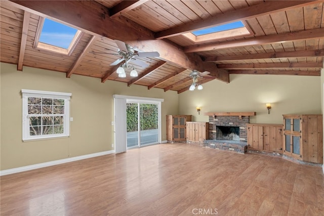 unfurnished living room with ceiling fan, wooden ceiling, light hardwood / wood-style flooring, a fireplace, and vaulted ceiling with skylight