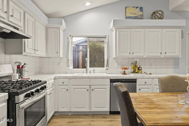 kitchen featuring backsplash, white cabinets, lofted ceiling, and appliances with stainless steel finishes