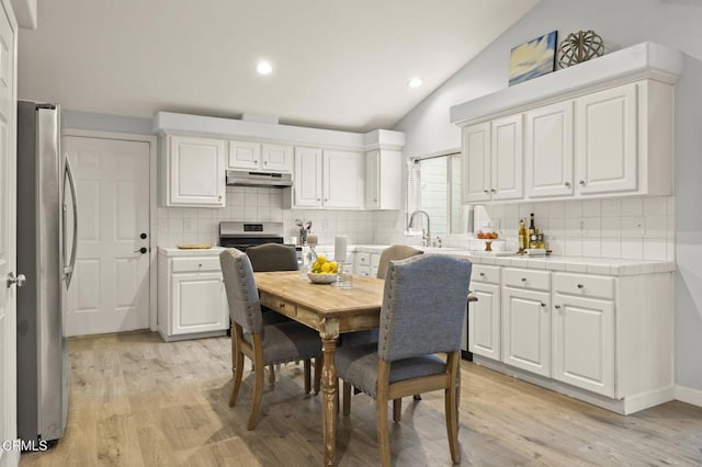 kitchen with lofted ceiling, white cabinets, appliances with stainless steel finishes, tasteful backsplash, and light hardwood / wood-style floors