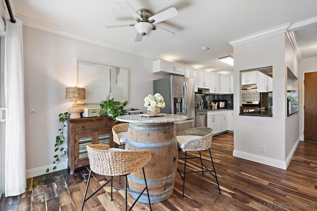 kitchen featuring appliances with stainless steel finishes, white cabinetry, decorative backsplash, dark hardwood / wood-style floors, and crown molding