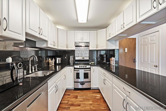 kitchen featuring appliances with stainless steel finishes, white cabinetry, dark stone countertops, light hardwood / wood-style floors, and sink