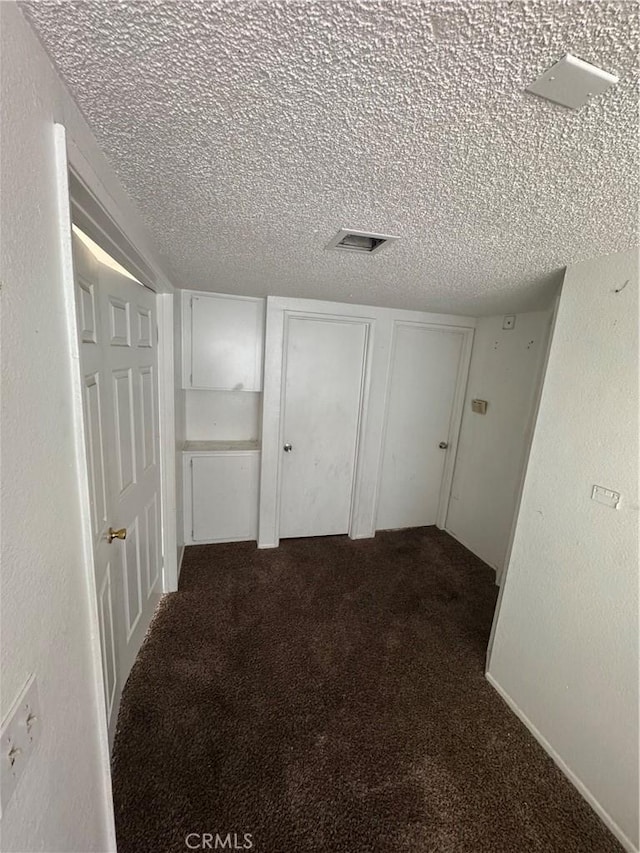 interior space featuring visible vents, dark carpet, a textured ceiling, and a textured wall