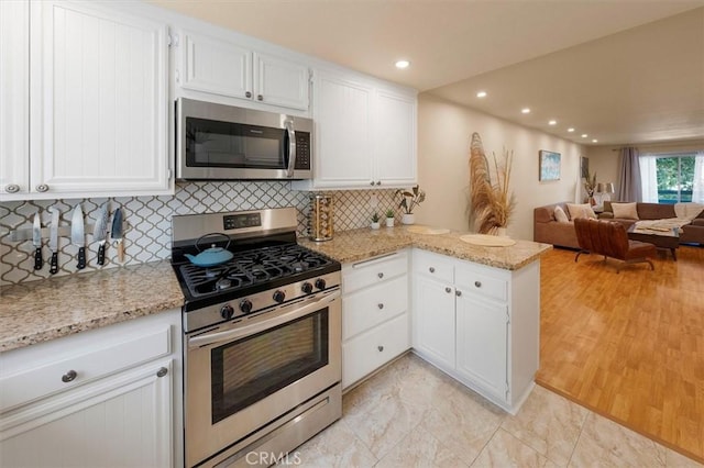 kitchen featuring kitchen peninsula, appliances with stainless steel finishes, light stone countertops, tasteful backsplash, and white cabinetry