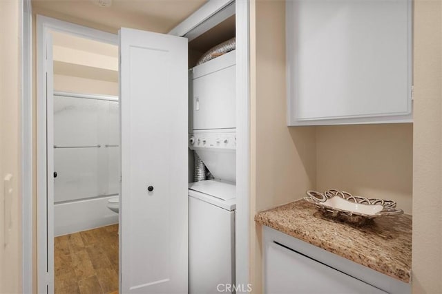 laundry room with light hardwood / wood-style flooring and stacked washing maching and dryer