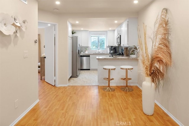 kitchen featuring kitchen peninsula, white cabinetry, stainless steel appliances, and light hardwood / wood-style floors