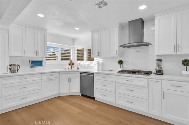 kitchen with stainless steel appliances, white cabinetry, and wall chimney range hood