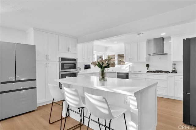 kitchen featuring a breakfast bar area, white cabinets, wall chimney exhaust hood, and light hardwood / wood-style floors