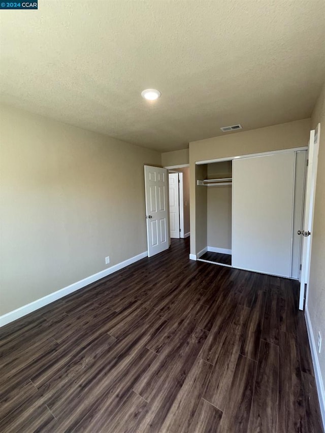 unfurnished bedroom with a textured ceiling, a closet, and dark hardwood / wood-style floors