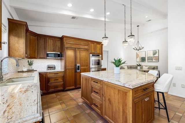 kitchen with sink, light stone countertops, appliances with stainless steel finishes, a kitchen island, and a breakfast bar area