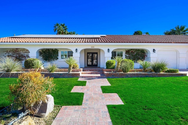 mediterranean / spanish house with solar panels, a garage, a front yard, and french doors