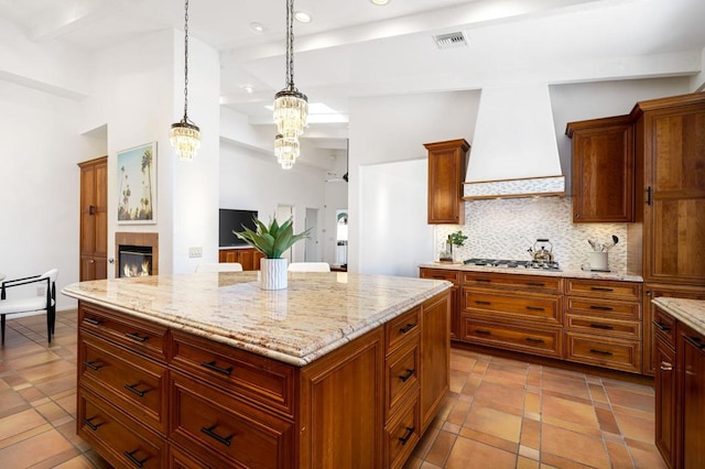 kitchen featuring a center island, backsplash, decorative light fixtures, stainless steel gas stovetop, and custom exhaust hood