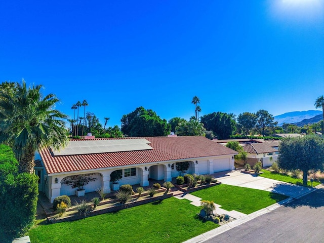 ranch-style house featuring a mountain view, a front lawn, a garage, and solar panels