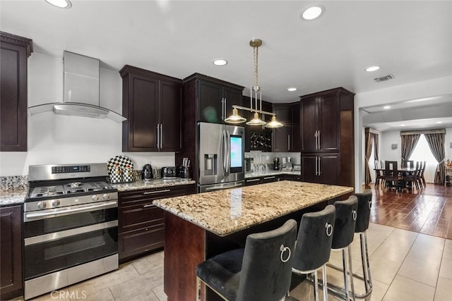 kitchen with a center island, hanging light fixtures, wall chimney range hood, light hardwood / wood-style floors, and appliances with stainless steel finishes