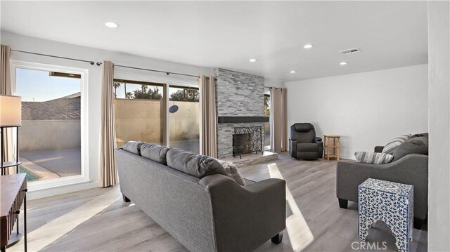 living room with a stone fireplace, plenty of natural light, and light wood-type flooring