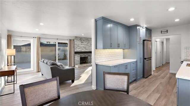 kitchen with a fireplace, stainless steel refrigerator, blue cabinets, backsplash, and light hardwood / wood-style floors