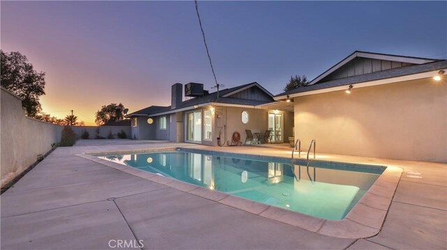 pool at dusk with cooling unit and a patio