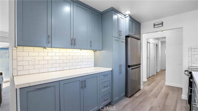 kitchen featuring stainless steel refrigerator, blue cabinets, backsplash, and light wood-type flooring