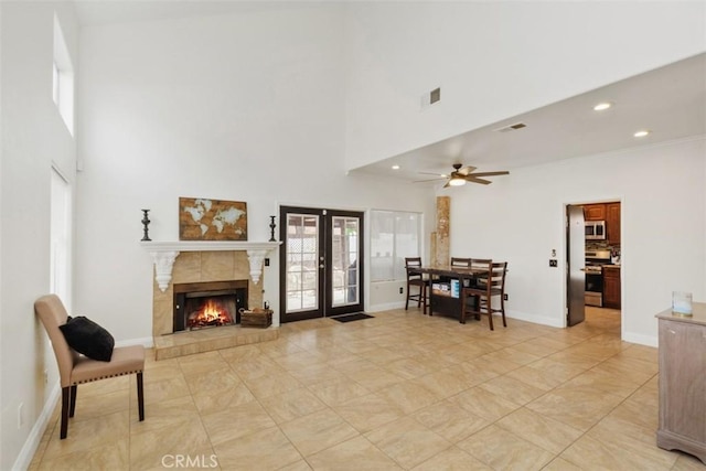 interior space featuring a fireplace, ceiling fan, french doors, and a high ceiling