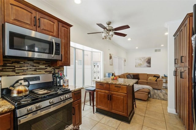 kitchen featuring decorative backsplash, ceiling fan, light stone countertops, light tile patterned flooring, and stainless steel appliances