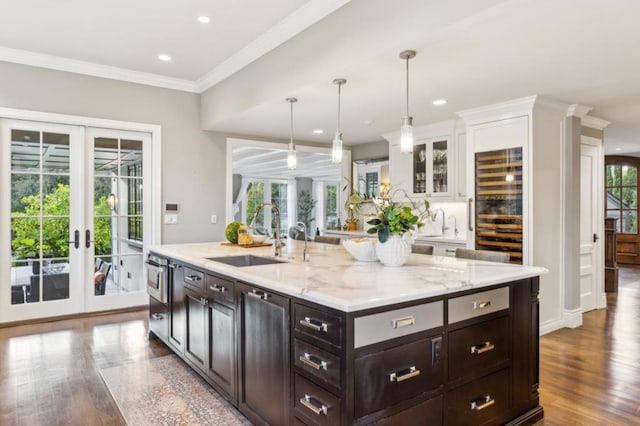 kitchen with french doors, sink, ornamental molding, an island with sink, and pendant lighting