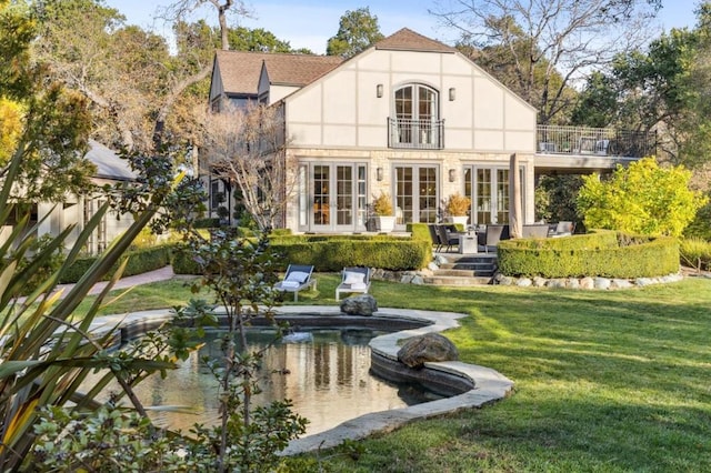 rear view of property featuring a lawn, french doors, a balcony, and a patio area