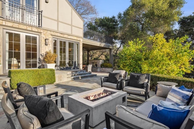 view of patio featuring an outdoor living space with a fire pit, french doors, and a balcony