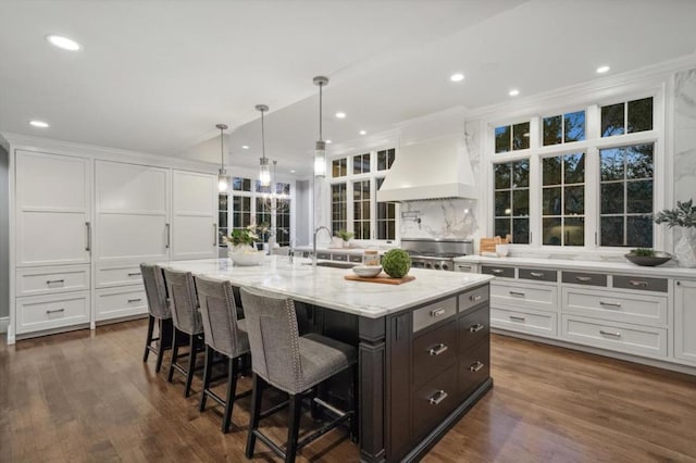 kitchen with a center island with sink, range, custom exhaust hood, and white cabinets