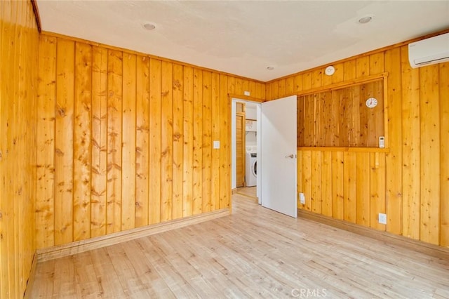 empty room featuring wooden walls, washer / clothes dryer, a wall mounted AC, and light hardwood / wood-style floors