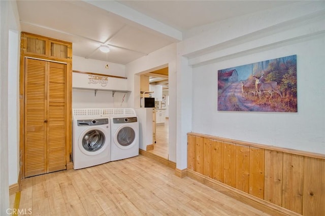 laundry area with wooden walls, washing machine and dryer, and light wood-type flooring