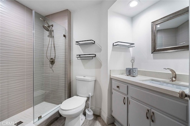 bathroom with a tile shower, vanity, wood-type flooring, and toilet