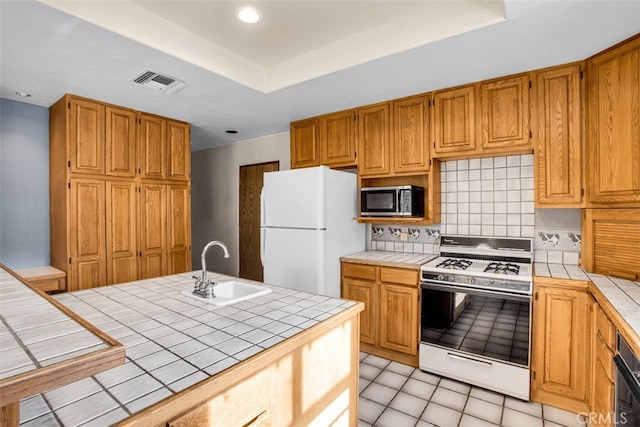 kitchen featuring backsplash, white appliances, a raised ceiling, sink, and tile counters