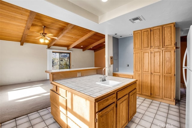 kitchen with ceiling fan, sink, tile countertops, a center island with sink, and light tile patterned floors