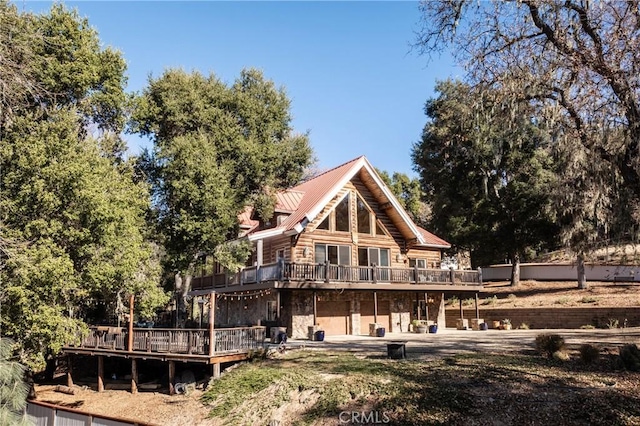 back of house featuring a patio, metal roof, log exterior, a deck, and stone siding