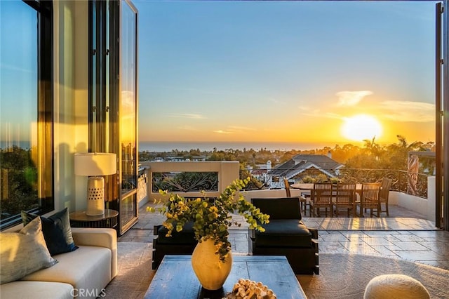 balcony at dusk with an outdoor living space, a patio area, and a water view