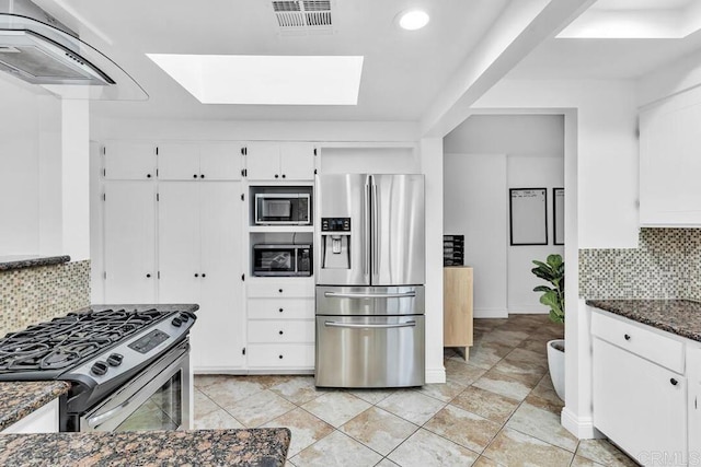 kitchen with backsplash, a skylight, stainless steel appliances, dark stone countertops, and white cabinets