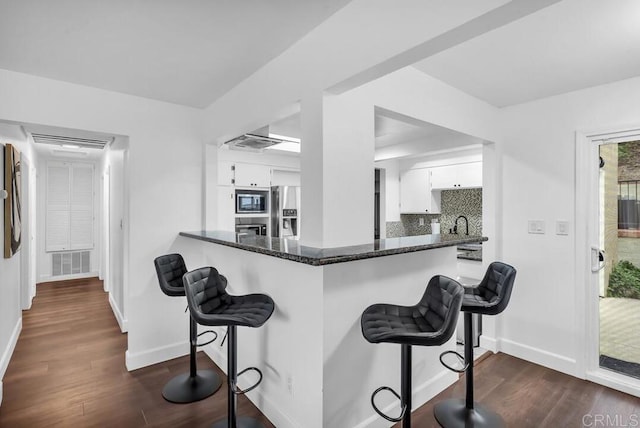 kitchen featuring kitchen peninsula, tasteful backsplash, stainless steel appliances, white cabinets, and dark hardwood / wood-style floors