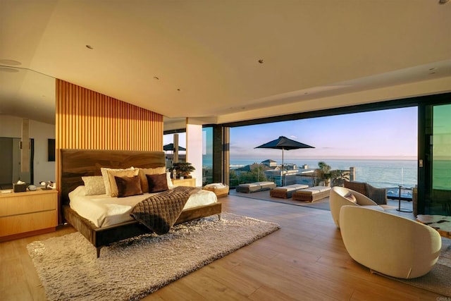 bedroom featuring a water view, wooden walls, and light hardwood / wood-style floors