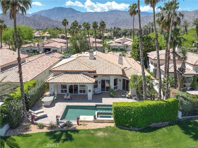 back of house with a patio, an in ground hot tub, and a mountain view