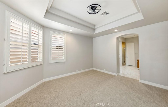 spare room featuring a tray ceiling and light colored carpet