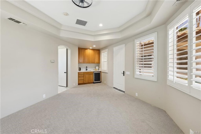 unfurnished living room featuring a raised ceiling, beverage cooler, and light carpet