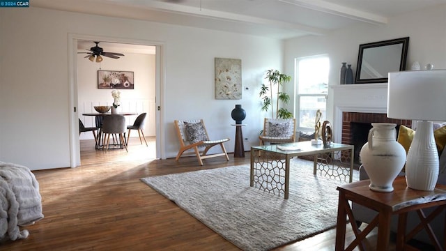 living room featuring beam ceiling, hardwood / wood-style flooring, a brick fireplace, and ceiling fan