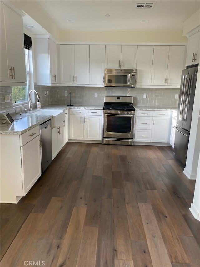 kitchen featuring appliances with stainless steel finishes, backsplash, light stone counters, white cabinets, and dark hardwood / wood-style floors