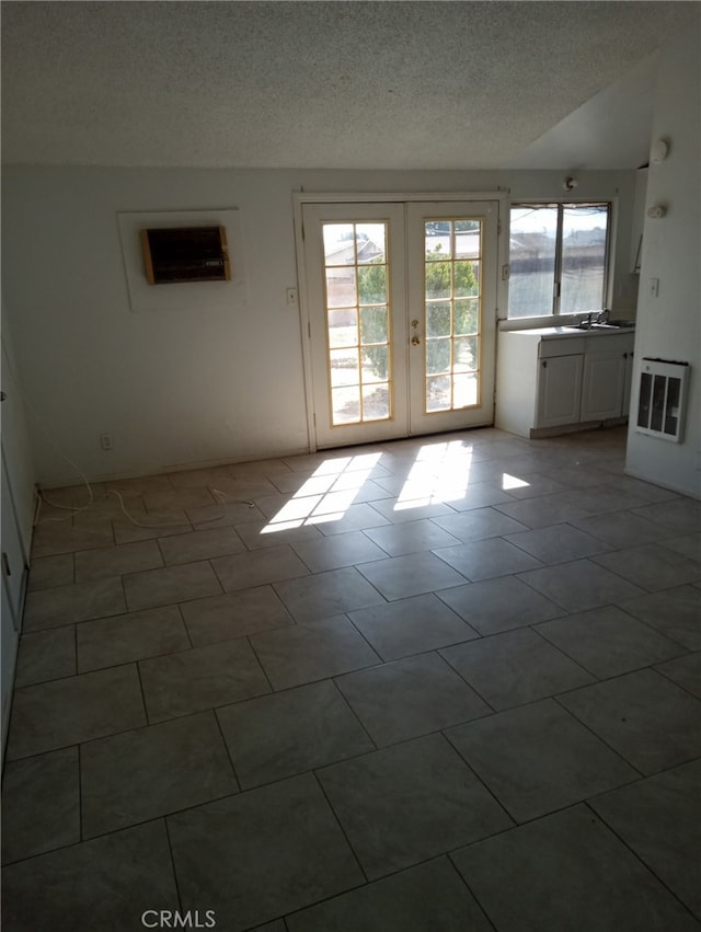 tiled empty room with french doors, plenty of natural light, a textured ceiling, and heating unit