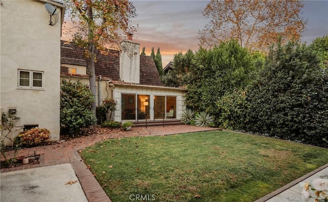 back house at dusk featuring a patio area and a lawn